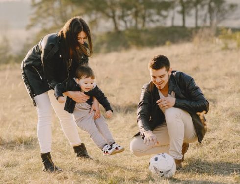 A happy family playing with a soccer ball in a grassy field on a sunny day.