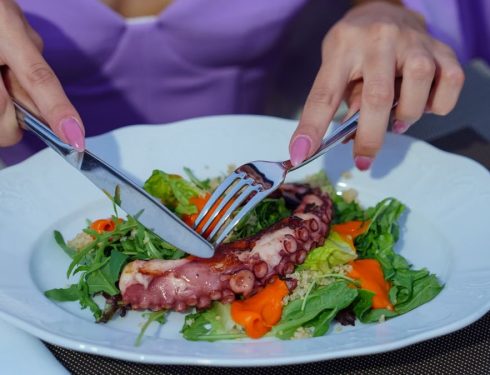 Woman enjoying an octopus salad with fresh greens outdoors. Vibrant and appetizing.